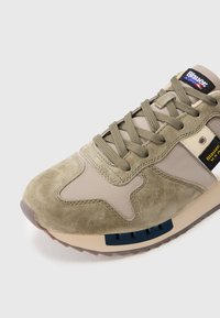 Μπεζ και ελιάς σουέτ αθλητικό παπούτσι με υφασμάτινα πάνελ, κορδόνια σε χρώμα ελιάς, ετικέτες με λογότυπο και μπεζ σόλα με λεπτομέρεια σε σκούρο μπλε.