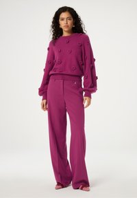 Fuchsia gebreide trui met textuurvolle bloemenaccenten en geribde manchetten, gecombineerd met fuchsia wijde broek. Zachte stof en een gladde afwerking.