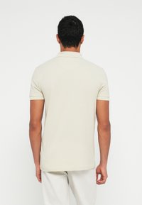 Polo de manga curta cor creme com gola de colarinho. Tecido liso, design minimalista e bainha reta.