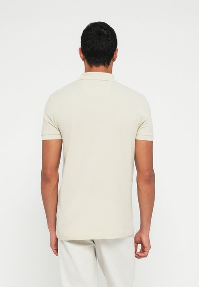 Polo à manches courtes de couleur crème avec un col rabattable. Tissu lisse, design minimaliste et ourlet droit.