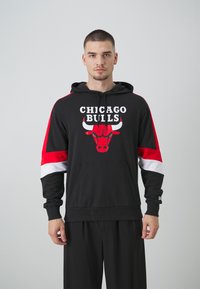 Felpa nera con cappuccio caratterizzata dal logo dei "Chicago Bulls" e una grafica di un toro, con dettagli a righe rosse e bianche sulle maniche e una tasca frontale.
