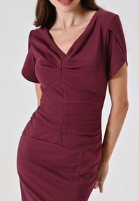 Bordeauxfarbenes Kleid mit V-Ausschnitt, kurzen Ärmeln und Raffung an Torso und Hüften. Glattes, enganliegendes Material mit Stretch.