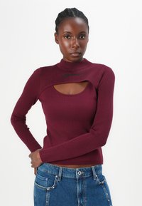 Bordeaux ribbeltrui met een hoge kraag en een ronde uitsnijding op de borst. Heeft lange mouwen en een slim fit.