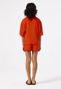 Top de lino naranja con mangas abullonadas y pantalones cortos a juego. La tela parece ligera y texturizada. Se lleva con sandalias planas.