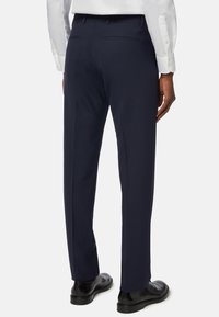 Námořnické kalhoty s úzkým střihem, se dvěma zadními kapsami a hladkou texturou. Nosič má na sobě černé boty.