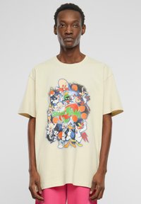 T-shirt oversize beige clair en coton, avec un graphique coloré de personnage de dessin animé "Space Jam" sur le devant.