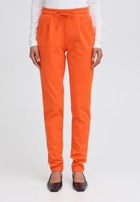 Oranje slim-fit sweatpants met zijzakken en een trekkoord tailleband, gecombineerd met zwarte puntige ballerina's.