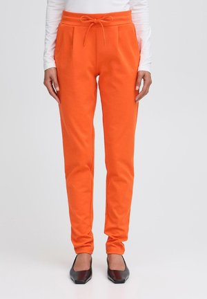 Oranžové slim-fit tepláky s bočními kapsami a stahovacími šňůrkami v pase, v kombinaci s černými balerínami s špičatou špičkou.