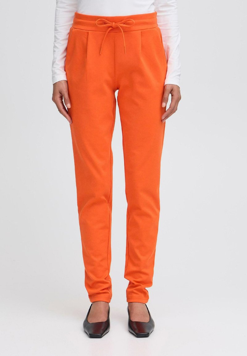 Oranje slim-fit sweatpants met zijzakken en een trekkoord tailleband, gecombineerd met zwarte puntige ballerina's.