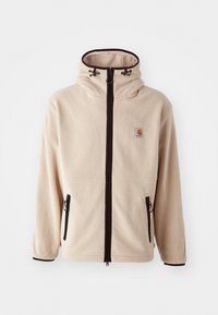 Chaqueta de forro polar beige con cuello alto, cremalleras negras y bolsillos laterales. Presenta un parche con logo en el pecho y un borde negro contrastante.