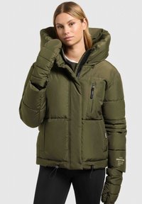 Doudoune vert olive avec une grande capuche, une poche poitrine zippée, des poignets élastiques et un ourlet à cordon de serrage ; texture matelassée sur l'ensemble.