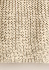 Kremasto obojena pletena tkanina s okomitim rebrastim uzorkom i vidljivim uzorcima uvezenih petlji pređe.