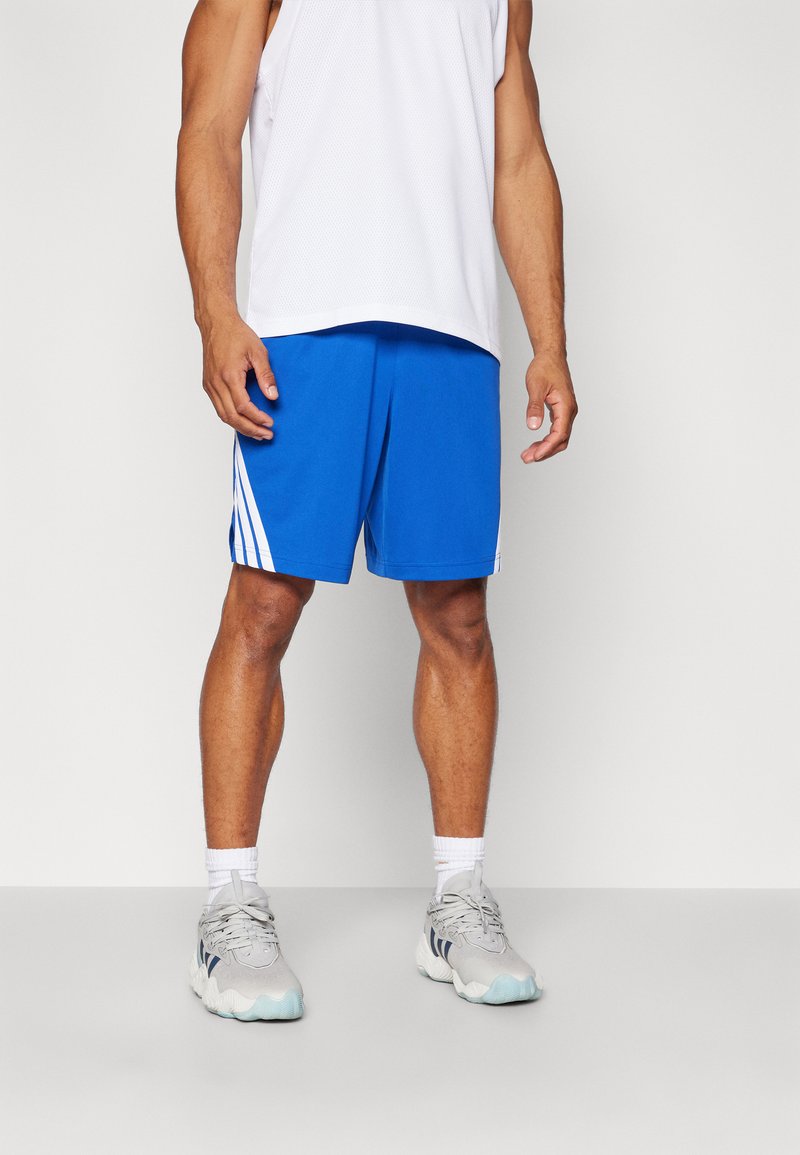 Blå atletiske shorts med hvite side-striper, laget av pustende stoff. Bært med en hvit ermeløs topp og grå joggesko.