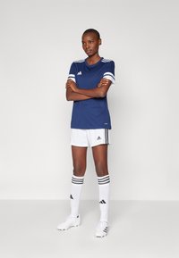Blå idretts skjorte med hvite striper, hvite shorts og svarte stripete sokker. Tilbehør inkluderer hvite fotballsko med svarte detaljer.