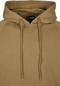 Mikina s kapucí v béžové barvě, vyrobená z měkké látky. Má stahovací šňůrky s kovovými koncovkami a žebrovaný výstřih a manžety na rukávech.
