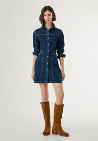 Denim dress with a collared neck, long sleeves, button front, and pockets. Dark blue color with visible stitching. Brown knee-high boots.