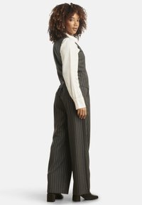 Pinstriped gray vest and wide-leg trousers, featuring a white shirt underneath. Materials appear textured; outfit styled with block-heeled boots.