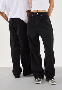 Černé džíny se širokými nohavicemi z denimu s vysokým pasem, vybavené zapínáním na knoflíky a zadními kapsami, doplněné o slip-on boty s kostkovaným vzorem.