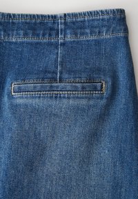 Tissu en denim d'une profonde teinte bleue avec une texture subtile, comportant une seule poche arrière avec une couture brodée le long de son bord.