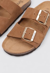 Sandales en daim brun à glissière avec deux sangles réglables dotées de boucles en ton or, semelle plate et semelle texturée pour le confort.