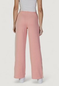 Pantaloni a gamba larga rosa chiaro con una consistenza morbida, vita elastica e spacchi laterali all'orlo, abbinati a calzature bianche.