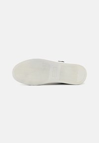 White rubber sole of a shoe featuring a textured surface, branding detail, and curved patterns for traction.