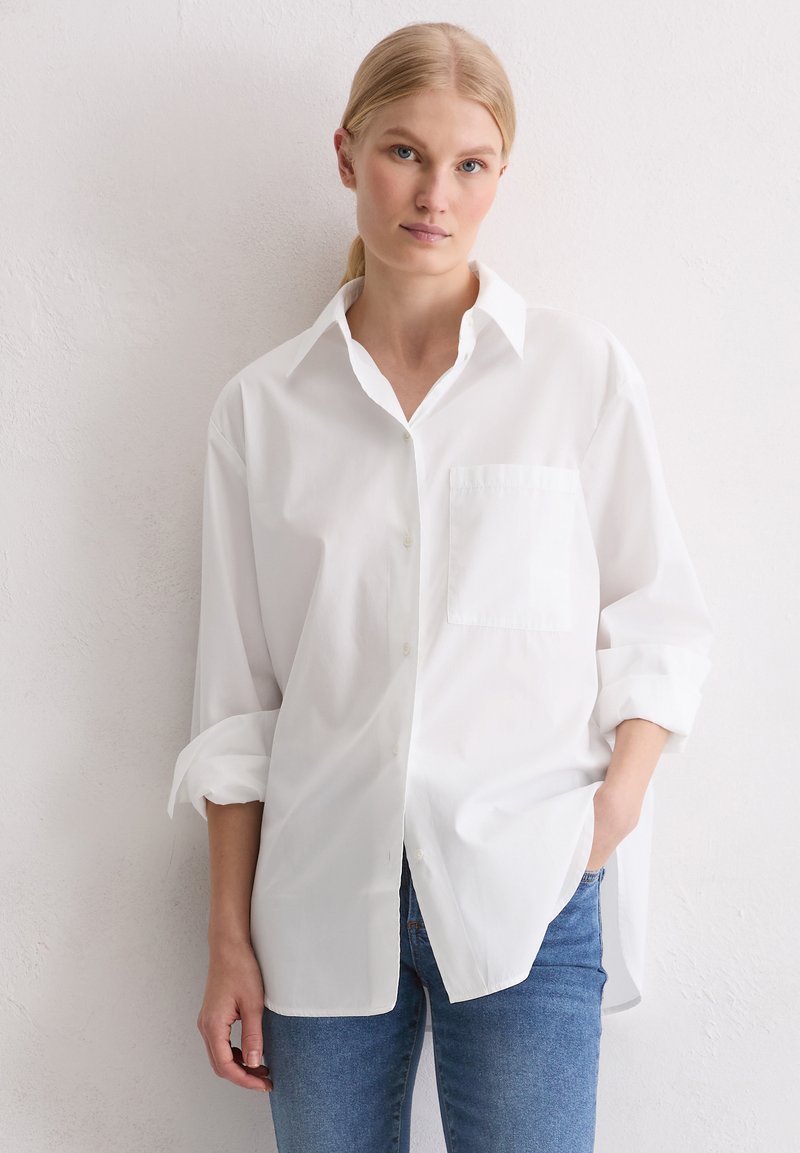 Witte button-up shirt met een klassieke kraag, lange mouwen, een enkele borstzak en een ontspannen pasvorm, gecombineerd met lichtblauwe jeans.