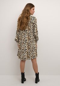 Leopardenmuster-Kleid mit langen Ärmeln, in Beige- und Brauntönen, seidenartige Textur, knielang, kombiniert mit schwarzen Knöchelstiefeln.