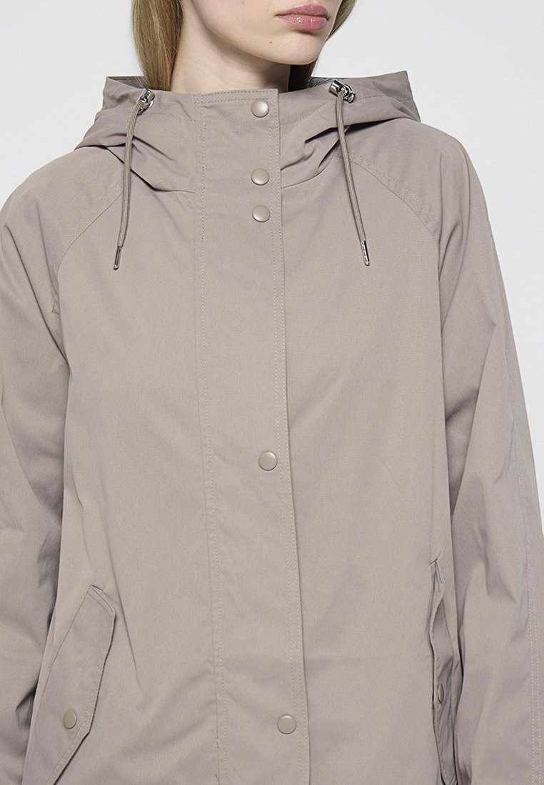 Veste beige clair avec capuche, boutons devant et poches latérales. Fabriquée en tissu lisse avec un design minimaliste et des cordons de serrage ajustables.