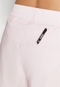 Lyserøde løbeshorts lavet af strækbart materiale, med en elastisk talje og en lille lomme med et sort "RUNNING" mærke.