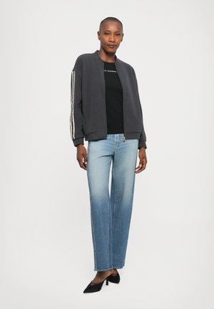 Gray bomber jacket with striped sleeves, black shirt, light blue straight-leg jeans, and black heels, standing against a white background.