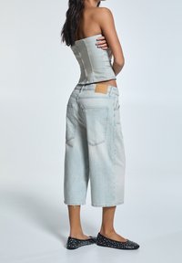 Top in denim azzurrino con corsetto e design strutturato, abbinato a jeans cropped larghi dello stesso colore. Scarpe ballerine nere con borchie completano l'outfit.
