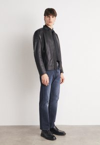 Black leather jacket with a stand-up collar, textured shoulders, and zippered closure. Worn with dark blue jeans and black shoes.