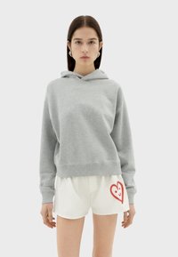 Grijze hoodie met een ontspannen pasvorm, gecombineerd met witte shorts met een rood hartontwerp. Gladde stoftextuur, casual stijl.