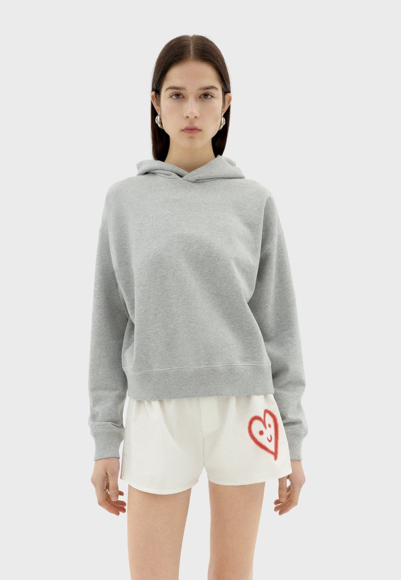 Grijze hoodie met een ontspannen pasvorm, gecombineerd met witte shorts met een rood hartontwerp. Gladde stoftextuur, casual stijl.