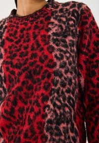 Suéter de estampado de leopardo rojo y negro, con una textura suave y peluda, cuello redondo y patrones contrastantes en diferentes tonos.