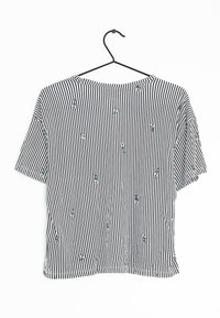 Black and white striped short-sleeve shirt featuring small floral embroidery and a round neckline, hanging on a black hook.
