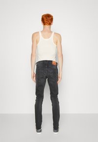 Mustad slim-fit teksad keskmise kõrgusega taljega, tagaküljel taskud ja pruun nahast brändiplekk. Kombineeritud valge kehaäriga ja sporditossudega.