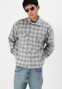 Grijze geruite shirt van zacht, gestructureerd materiaal met twee voorzakken, knoopsluiting en een relaxed fit, gecombineerd met blauwe spijkerbroeken.
