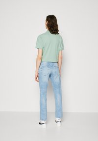 Lys grønn avkortet t-skjorte, løs passform, kombinert med lyseblå rette jeans. Antrekket inkluderer hvite joggesko med svarte detaljer.