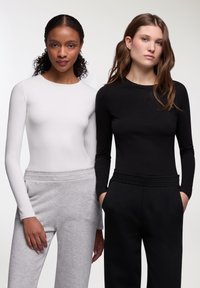 Magliette a manica lunga in tessuto elastico bianco e nero, abbinate a pantaloni della tuta grigi e neri. Design aderente con scollatura rotonda e cinture elastiche.