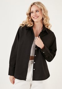 Black button-up shirt with long sleeves, collar, and white buttons. Fabric appears lightweight with a slightly textured finish.
