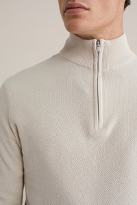 Cremfarbener Pullover mit Viertelreißverschluss, strukturiertem Strick, geripptem Kragen und silbernem Reißverschluss, der eine enge Passform und subtile Details aufweist.