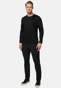 Melna garenruka T-krekls, izgatavots no mīkstas auduma, apvienots ar tumšām biksēm un melniem sporta apaviem, demonstrējot vienkāršu un elegantu dizainu.