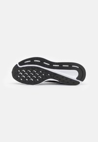 Semelle de chaussure de sport en noir et blanc, avec une surface en caoutchouc texturé présentant un motif de semelle détaillé et un bord latéral lisse et courbé.