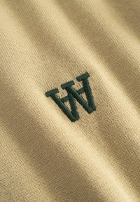Gros plan sur un tissu beige avec des lettres superposées "W" et "H" brodées en vert foncé sur une surface tricotée douce.