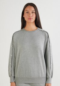 Grå sweatshirt lavet af blødt stof, med rund halsudskæring, knapdetaljer på skuldrene og ribbede manchetter. Casual pasform med tekstureret detalje.