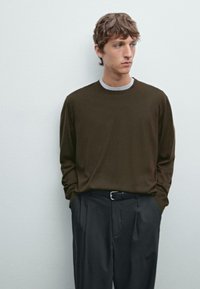 Braunes Langarmhemd mit Rundhalsausschnitt, über einem grauen Shirt. Kombiniert mit dunklen Hosen und einem schwarzen Gürtel. Glatte Textur.