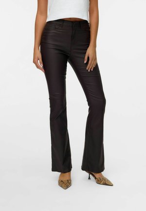 Personne portant un pantalon marron foncé ajusté avec une légère évasement, un haut court blanc et des talons pointus à motif peau de serpent.