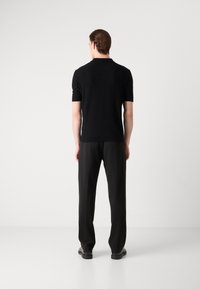 Zwart poloshirt met korte mouwen en een gestructureerde afwerking, gecombineerd met rechte zwarte broeken en zwarte schoenen, gezien vanuit de achterkant.